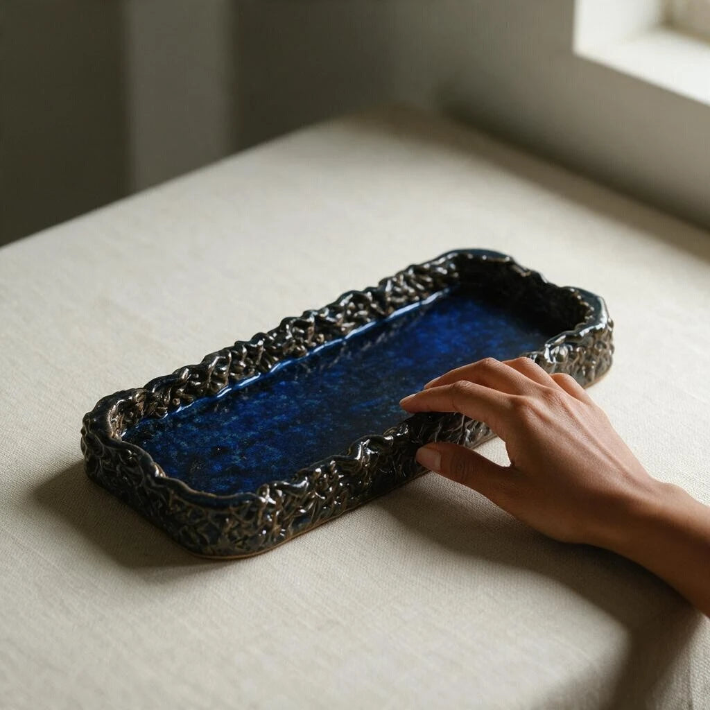 Hand touching the edge of a glossy midnight blue 3D printed ceramic tray with textured woven rim on a beige tablecloth #color_sapphire blue