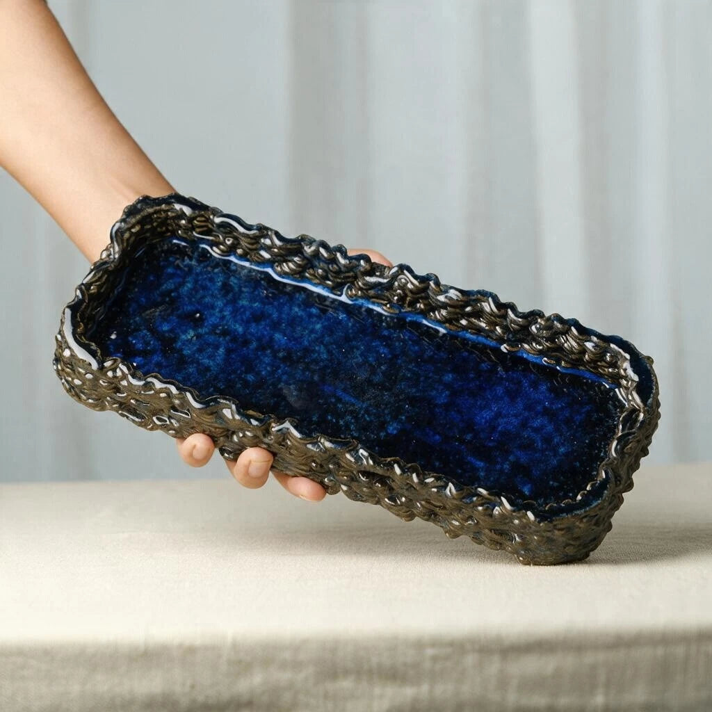 Hand holding a rectangular glossy midnight blue 3D printed ceramic decorative tray showcasing its textured outer weave #color_sapphire blue