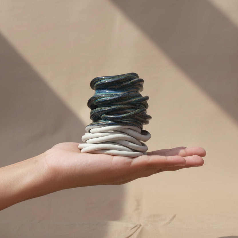 A hand holding a small ceramic decorative object, with the top half in dark blue-green and the bottom half in white, against a beige fabric backdrop #color_sapphire blue