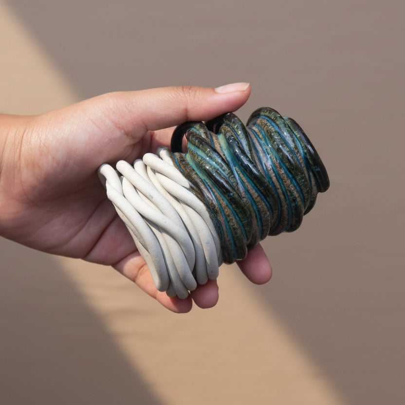 A hand holding a coiled ceramic decorative object, blue and white, set against a neutral beige fabric background #color_sapphire blue