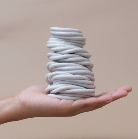 A hand holds a small 3d printed ceramic vase against a backdrop of brown paper #color_white