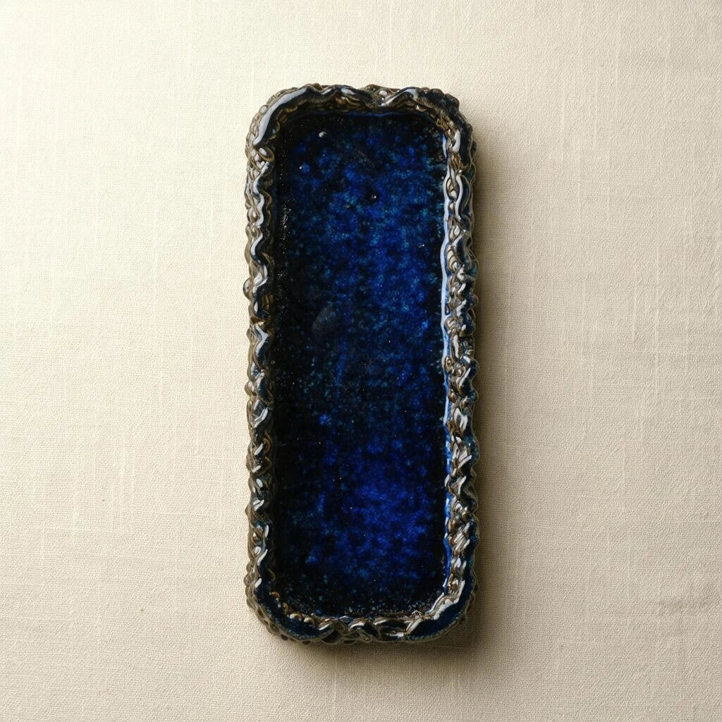 Top-down view of a rectangular 3D printed ceramic tray in glossy midnight blue with intricate woven border. #color_sapphire blue