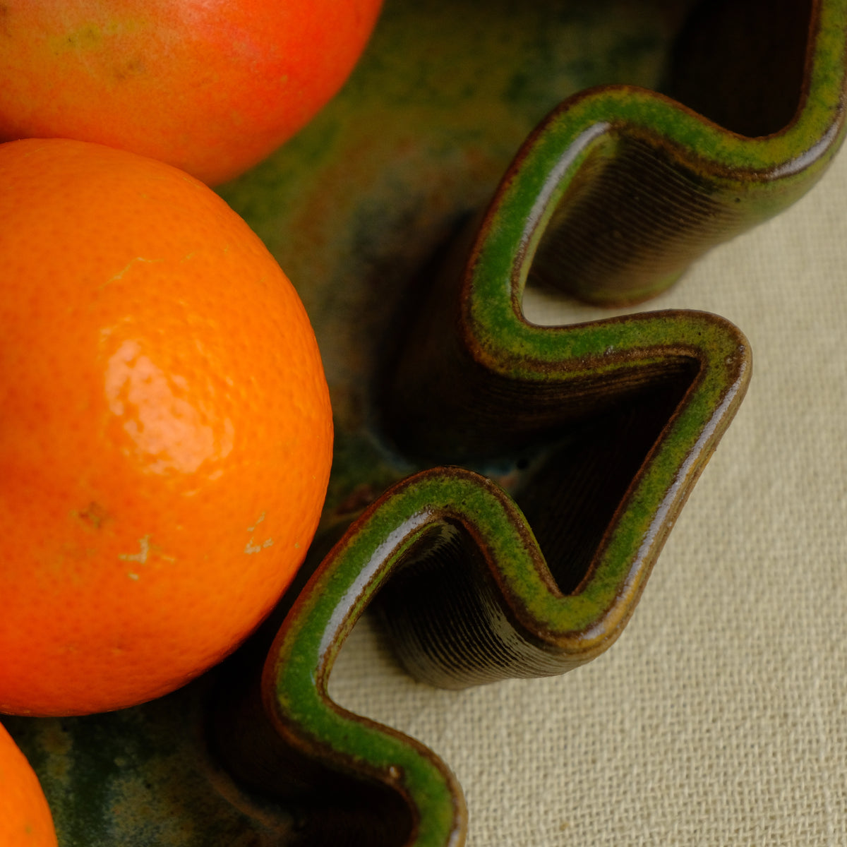 Green ceramic tray close up image. The glossy glaze is breaks revealing the clay body underneath. #color_olive green