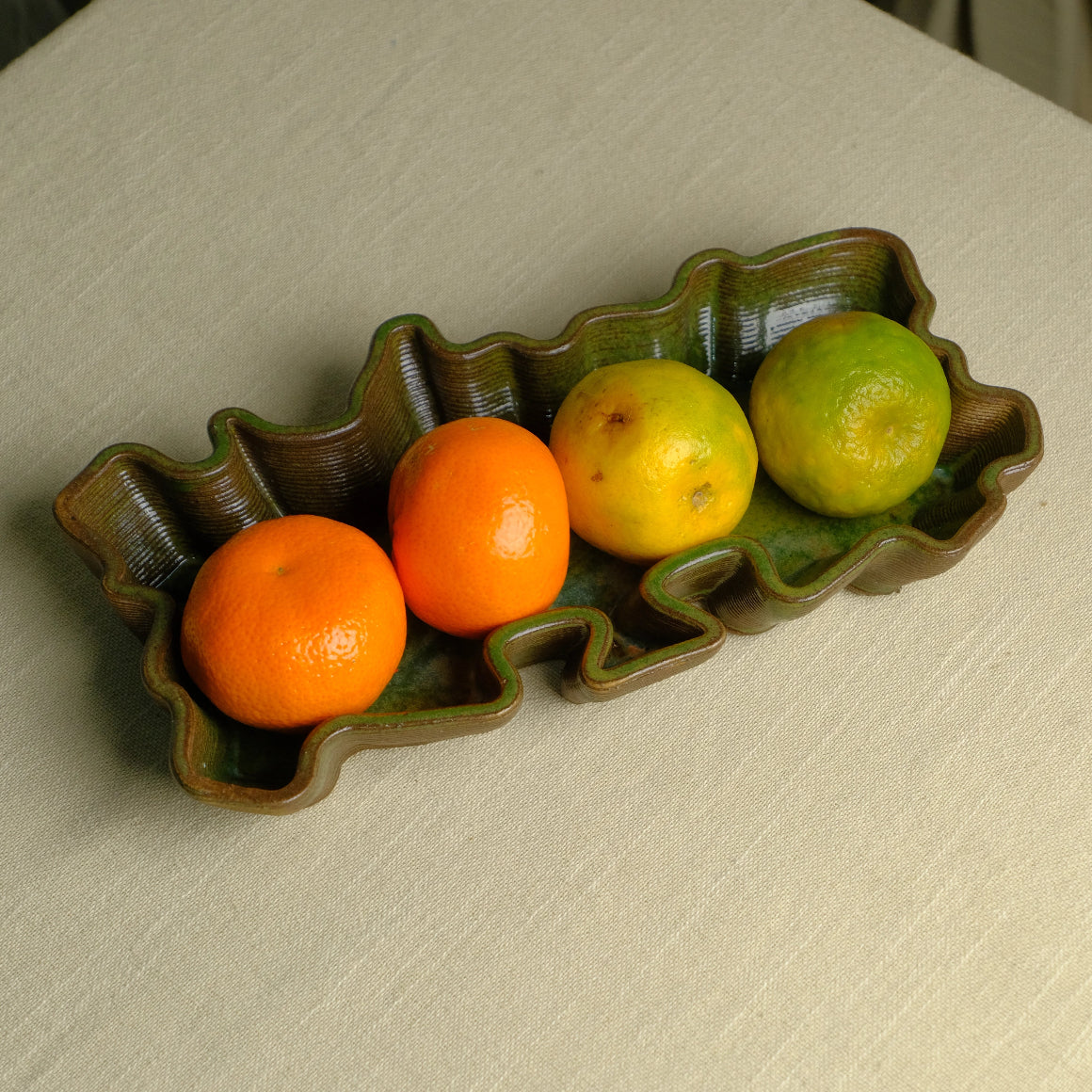 Olive green ceramic tray kept on a light surface. Oranges and mandarins kept inside tray. #color_olive green