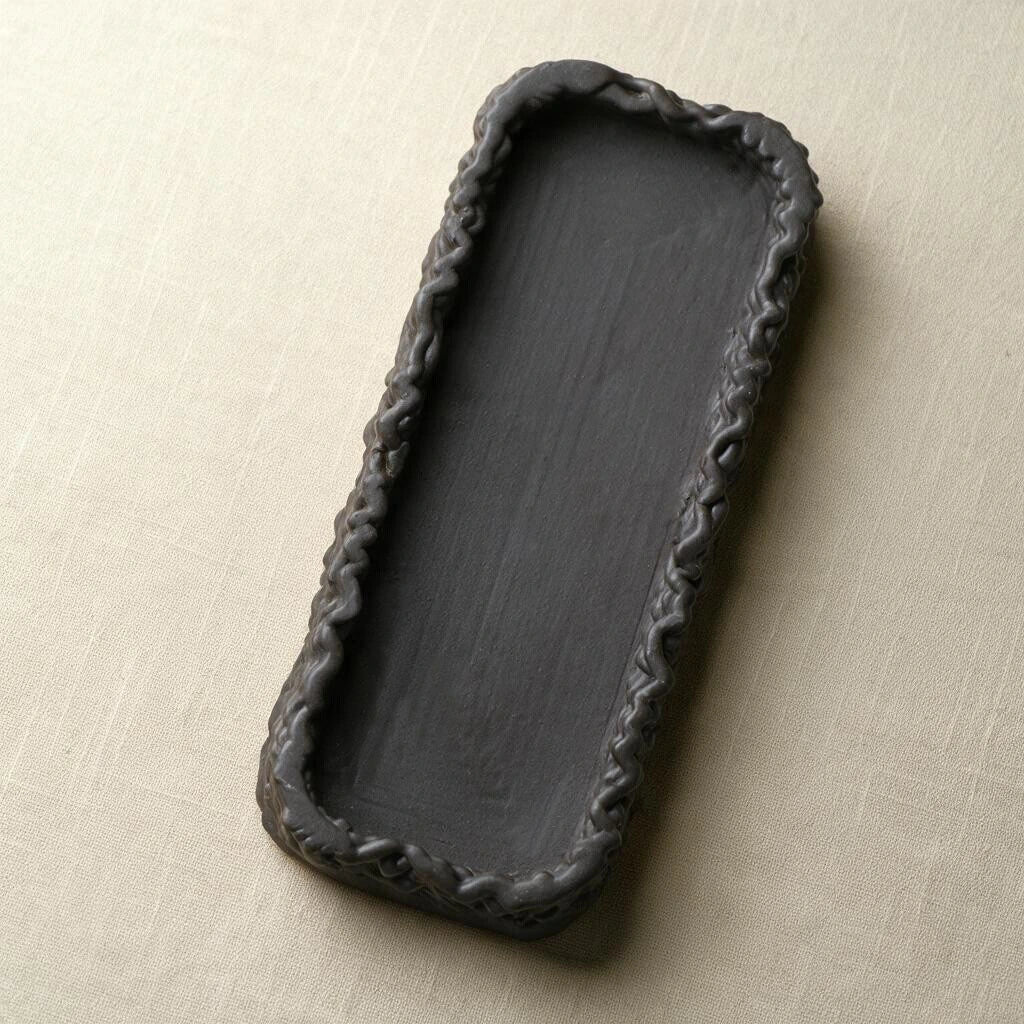 Angled top-down view of a rectangular matte black 3D printed ceramic tray with textured woven border #color_black