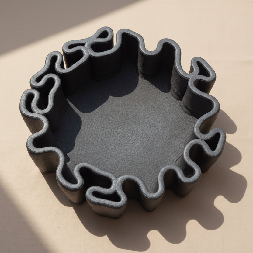 A dark gray ceramic tray, bonsai planter or a decorative pot with a wavy, scalloped edge, photographed from directly above. 
