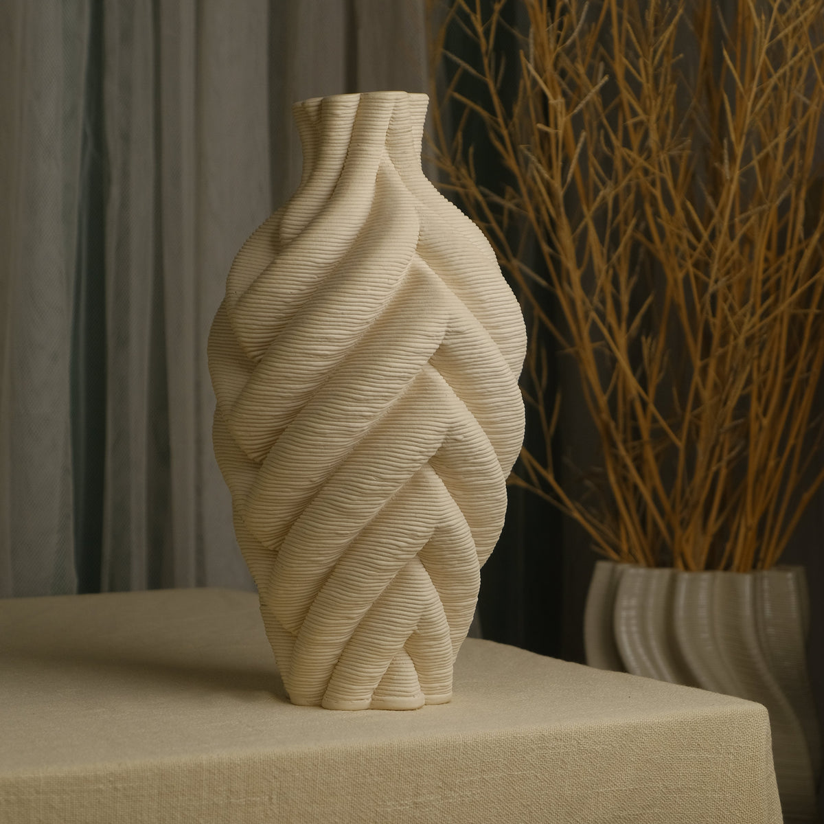 A sculptural beige ceramic vase kept on a fabric draped table 