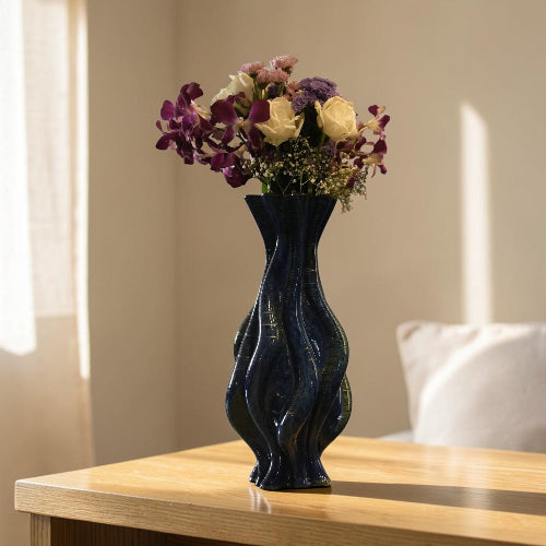 A navy blue wavy ceramic vase filled with a bouquet of purple, cream, and pink flowers, set on a light wood table in a softly lit room #color_sapphire blue