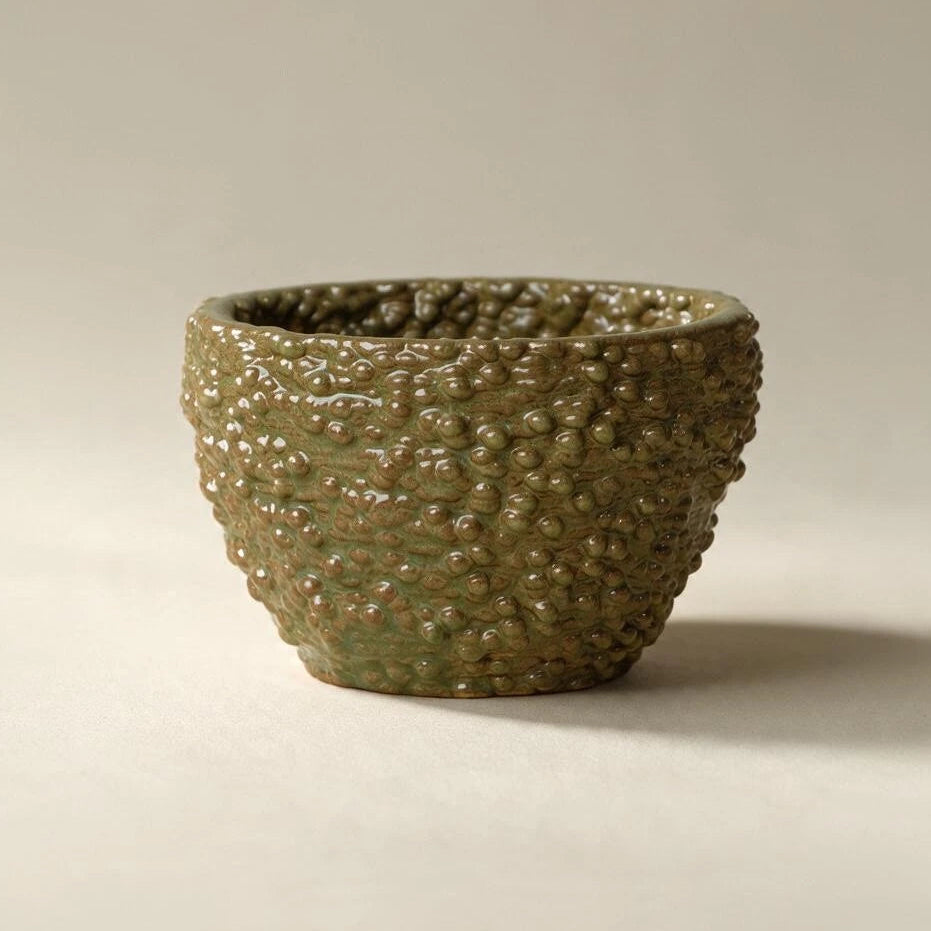 A textured ceramic bowl with a glossy olive-green and brown mottled glaze, set against a plain light beige background. #color_olive green