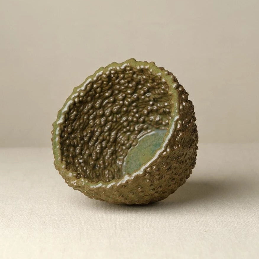 A 3d printed and hand painted ceramic bowl with a textured mulberry exterior and a smooth, glossy interior, shown on a neutral beige background. #color_olive green